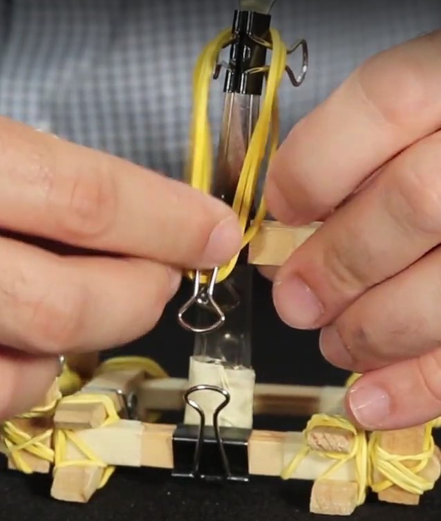 Passe os mesmos três elásticos pela haste de fora do Binder clip conectado na madeira.