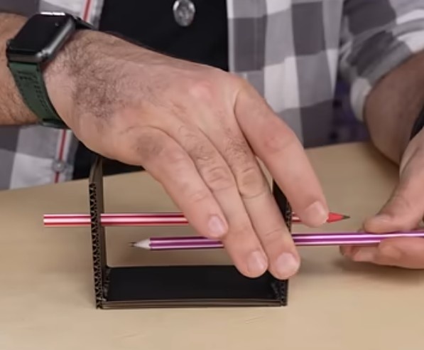 Atravesse um lápis por 1 furo de um lado e 1 furo do outro lado, de forma que fique nivelado. Repita o processo para o outro lápis, mas com sentido contrário, de forma que o fundo dos lápis fique opostos.