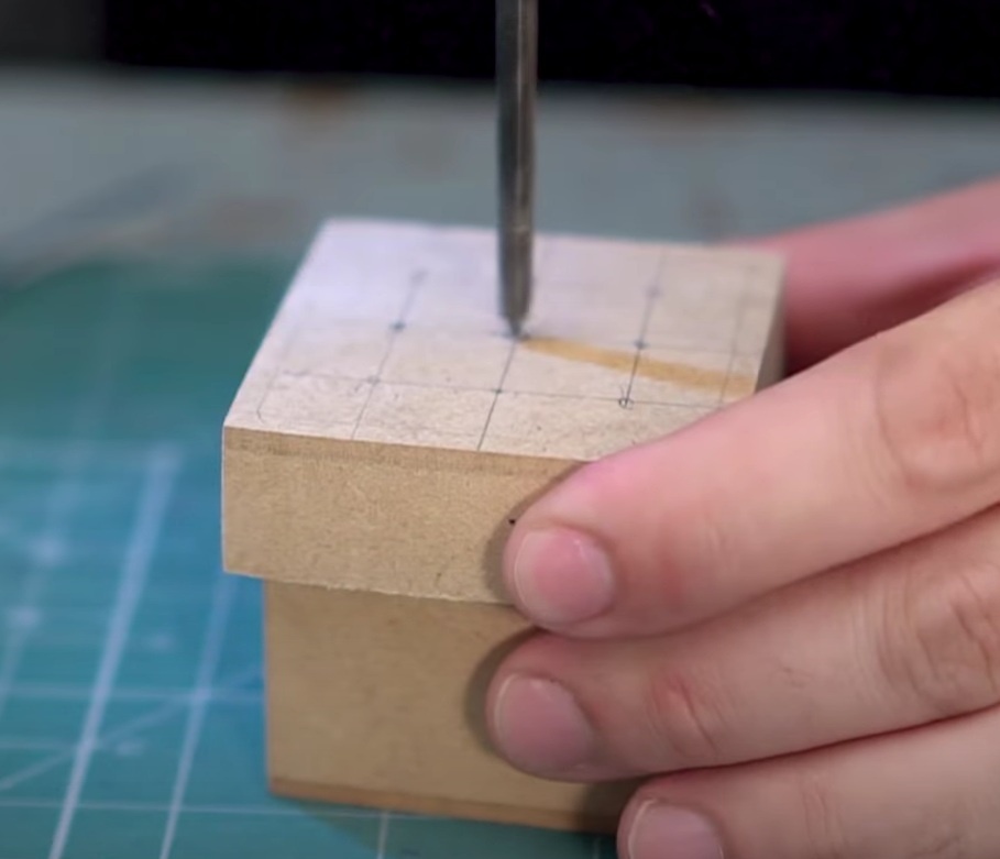 Utilizando a furadeira com a broca de 5mm, com cuidado e sem usar muita força, faça os 7 furos nos locais marcados da tampa.