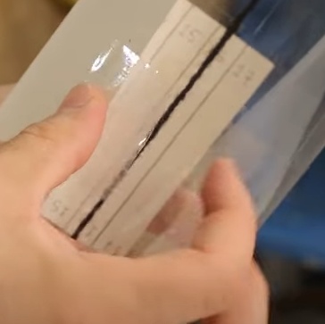 Utilizando uma fita adesiva, fixe a folha com as marcações mais ou menos no meio da garrafa, mantendo os números voltados para dentro e como se a folha fosse enrolar a garrafa novamente (agora só cobrindo metade do perímetro). Mantenha as linhas marcadas na folha bem alinhadas com o comprimento da garrafa, olhe através da garrafa e confira se as linhas se alinham com o barbante que está passando ali dentro.