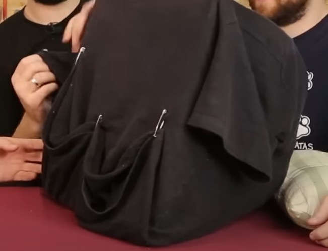 Dobre da melhor forma possível o “excesso” de camiseta e as mangas da camiseta. Usando os alfinetes de segurança prenda tudo debaixo da base.